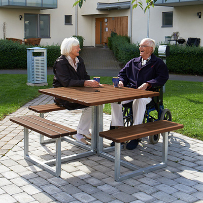 Picnic table with elderly couple enjoying a chat and the surrounding area, which looks residential.